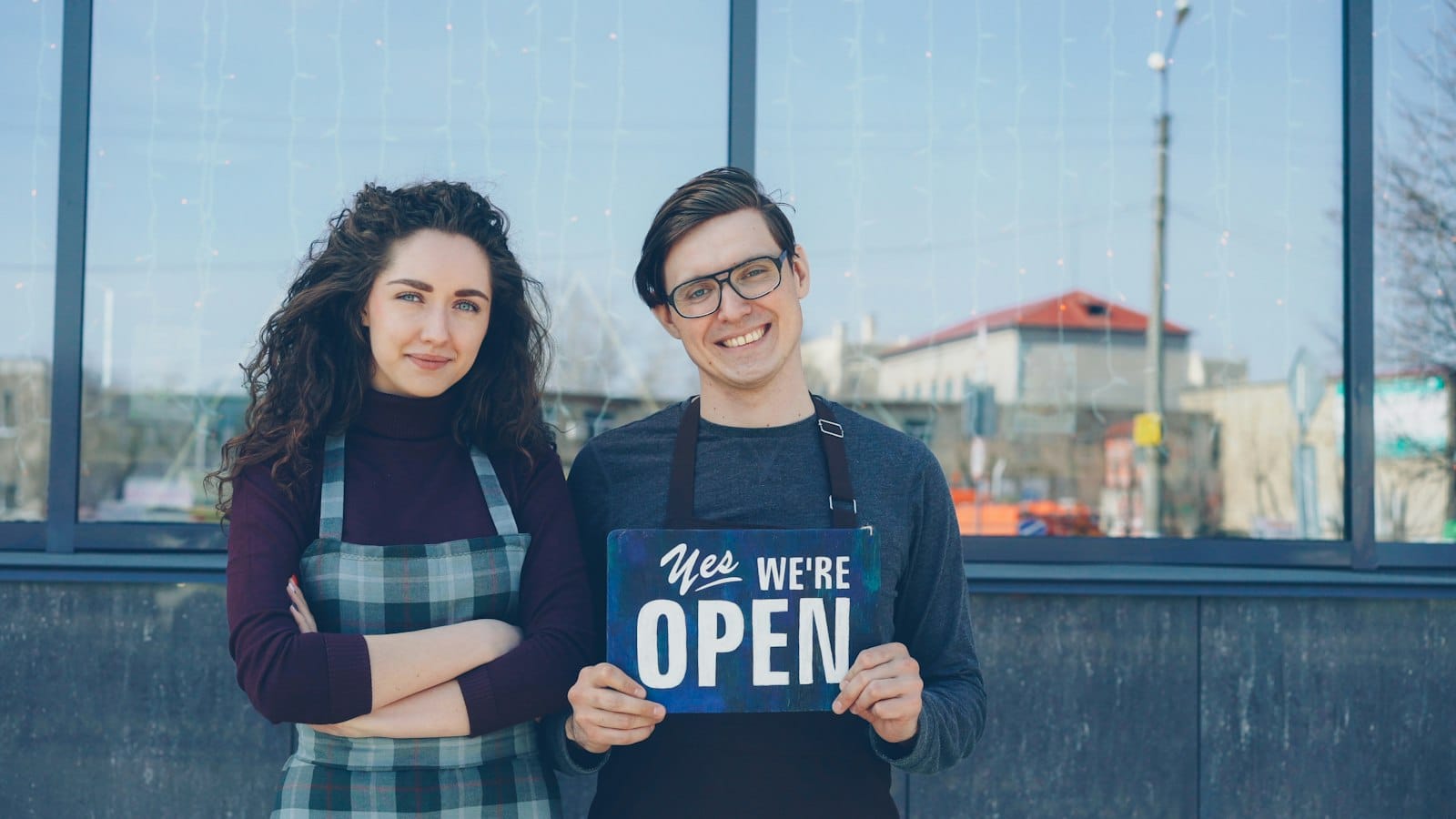 Two business partners holding a 'we are open' sign outside their new restaurant
