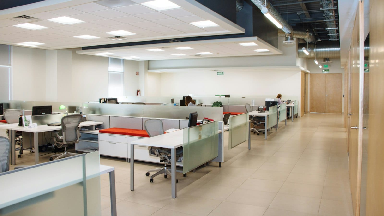 An open-plan office with rows of white desks and glass partitions