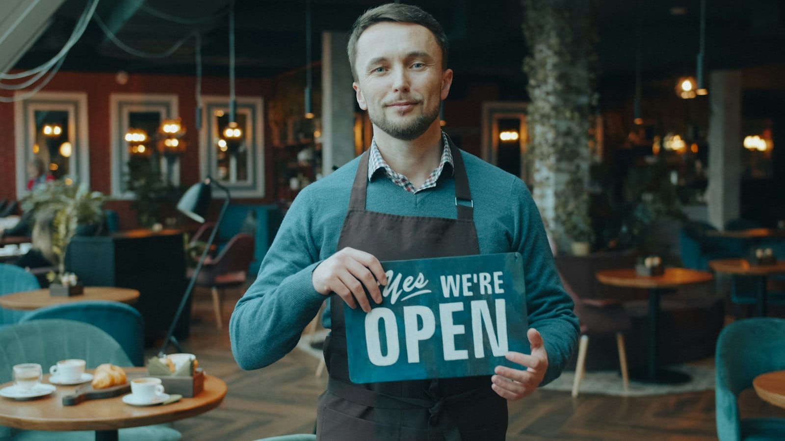 A café owner in an apron holding an open sign