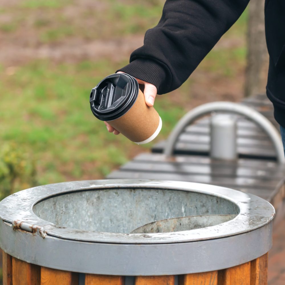 Close up hand throwing empty paper disposable coffee cup in recycling bin. Eco friendly approach concept.